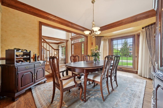 dining area featuring crown molding, light wood-style flooring, stairway, and a chandelier