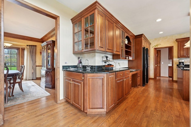 kitchen with a sink, light wood-style flooring, glass insert cabinets, baseboards, and brown cabinets