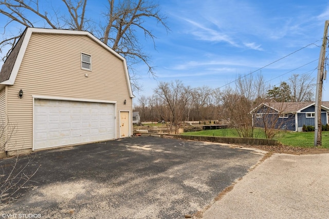 view of home's exterior featuring an attached garage, a gambrel roof, and aphalt driveway