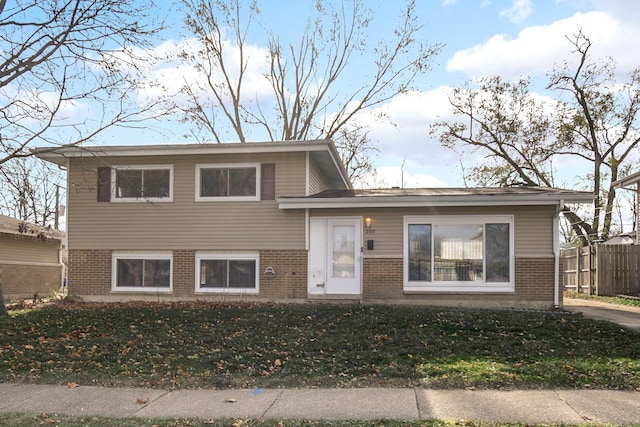 tri-level home featuring fence, a front lawn, and brick siding