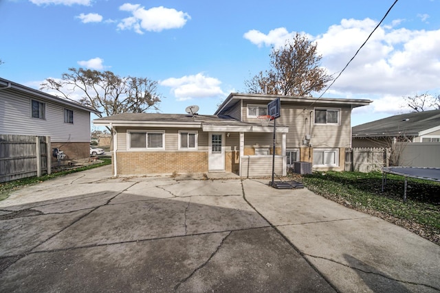 rear view of house featuring a trampoline, a patio, cooling unit, brick siding, and fence