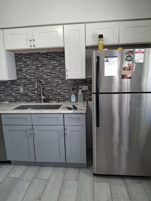 kitchen featuring a sink, decorative backsplash, freestanding refrigerator, and white cabinets