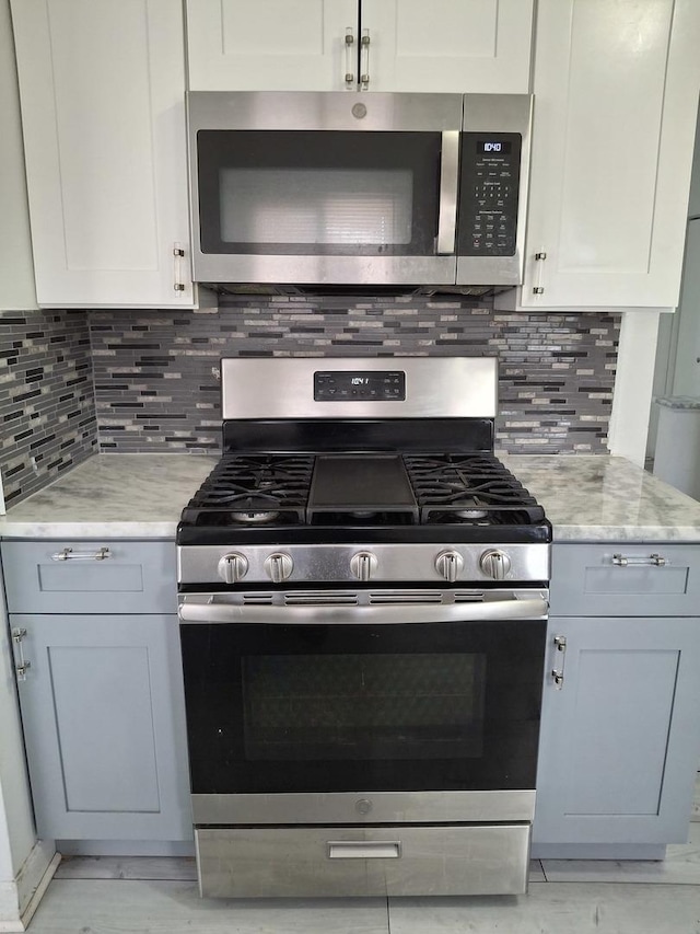kitchen featuring tasteful backsplash, light stone countertops, white cabinetry, and appliances with stainless steel finishes