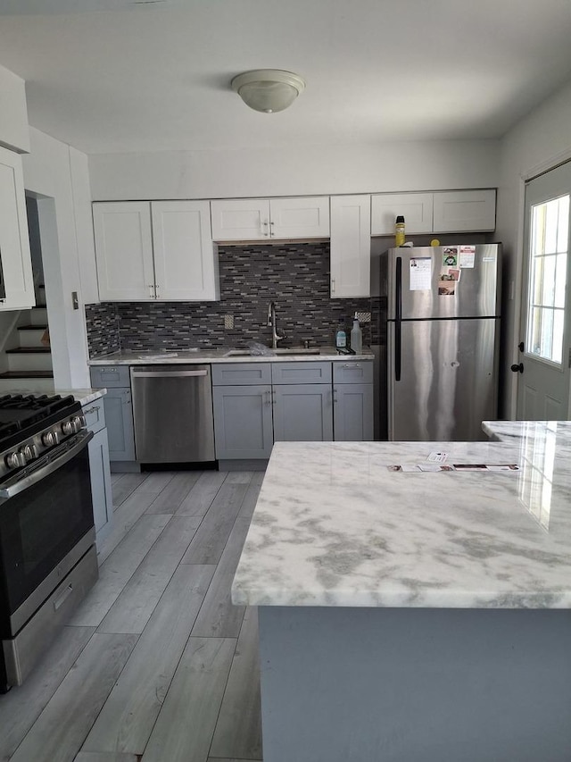 kitchen featuring a sink, light wood-type flooring, appliances with stainless steel finishes, white cabinetry, and backsplash