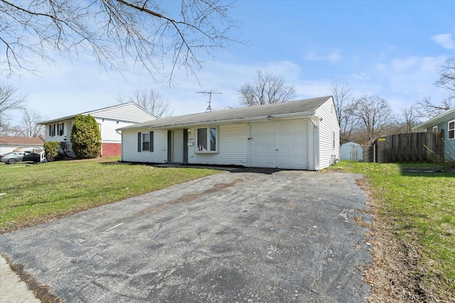 ranch-style home featuring an attached garage, fence, a front lawn, and aphalt driveway