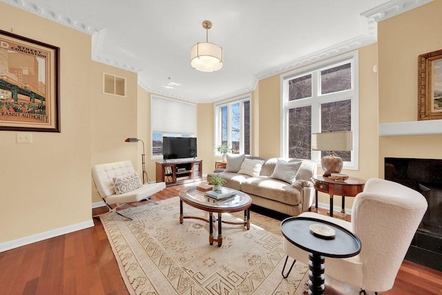 living area featuring baseboards, crown molding, wood finished floors, and visible vents