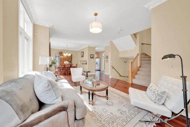 living area featuring baseboards, an inviting chandelier, wood finished floors, stairs, and ornamental molding