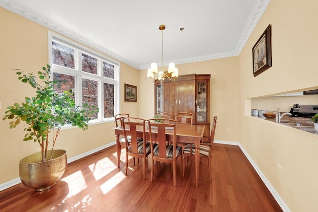 dining space featuring wood finished floors, ornamental molding, baseboards, and a notable chandelier