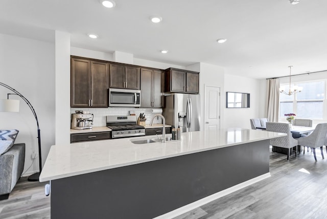 kitchen with dark brown cabinetry, a chandelier, light wood-style floors, stainless steel appliances, and a sink
