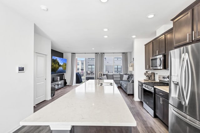 kitchen featuring a sink, open floor plan, appliances with stainless steel finishes, dark brown cabinetry, and wood finished floors