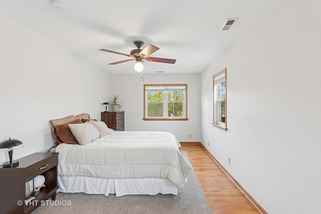 bedroom featuring ceiling fan, visible vents, baseboards, and light wood-type flooring