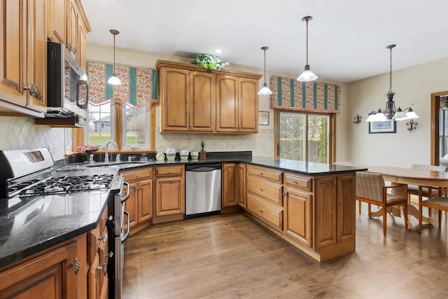 kitchen featuring a peninsula, brown cabinetry, appliances with stainless steel finishes, a sink, and wood finished floors
