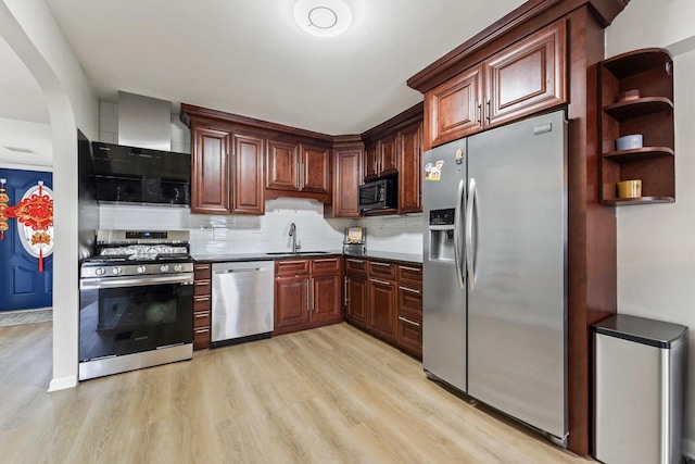 kitchen featuring dark countertops, wall chimney exhaust hood, stainless steel appliances, light wood finished floors, and a sink