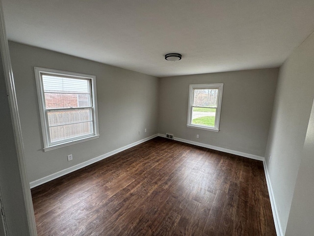 empty room with baseboards, dark wood-style flooring, and visible vents