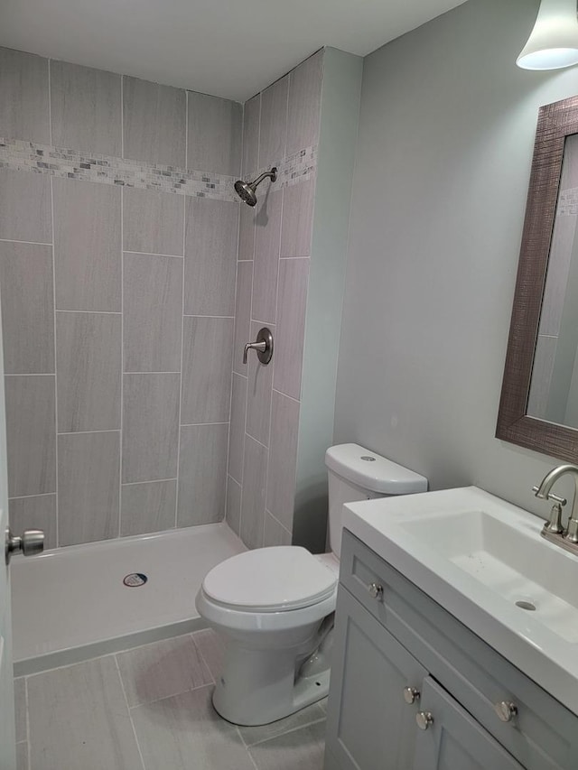full bath featuring toilet, tiled shower, vanity, and tile patterned flooring