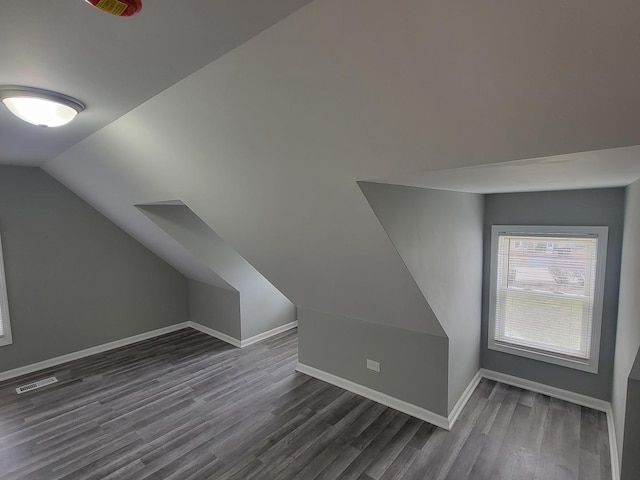 additional living space featuring visible vents, baseboards, vaulted ceiling, and dark wood-style floors