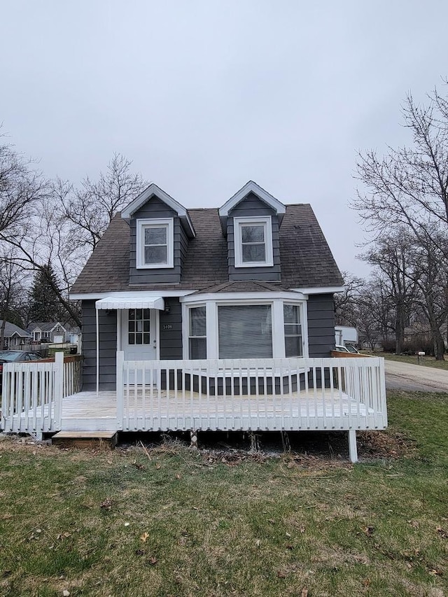 new england style home with a shingled roof, a front yard, and a deck