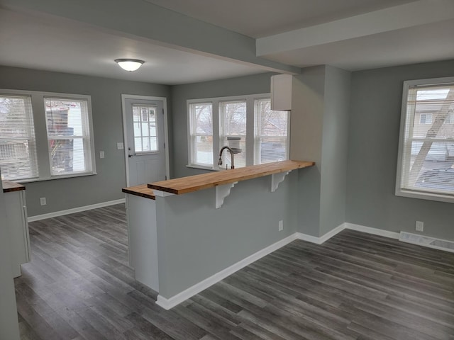 kitchen featuring baseboards, wood counters, visible vents, a kitchen bar, and dark wood finished floors