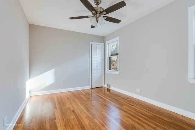 empty room with ceiling fan, light wood finished floors, baseboards, and visible vents
