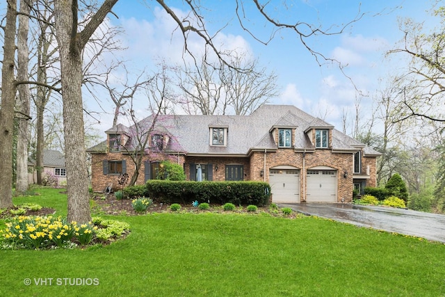 french country home with a garage, a front yard, driveway, and brick siding