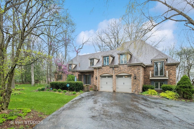 french country style house featuring an attached garage, driveway, a front lawn, and brick siding