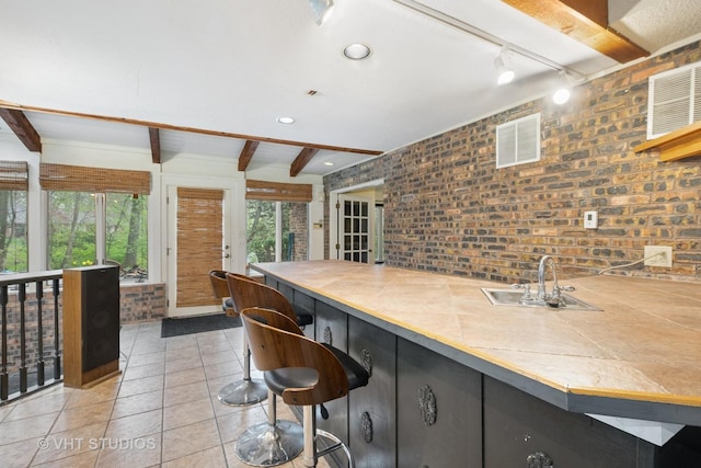 kitchen with a sink, tile countertops, light tile patterned floors, beamed ceiling, and visible vents