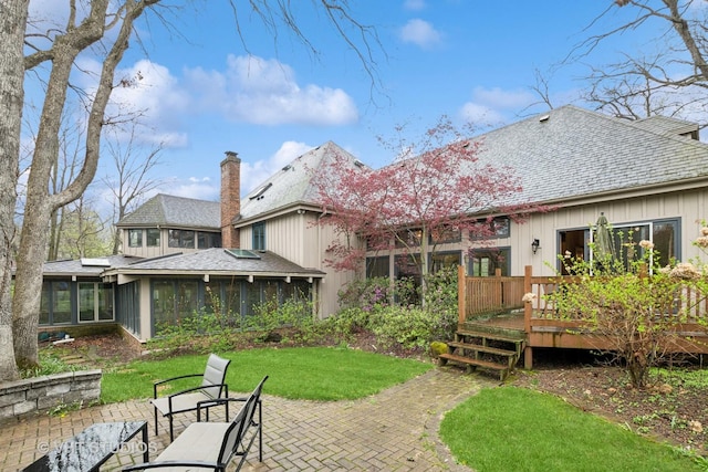 back of house featuring roof with shingles, a sunroom, a deck, a patio, and a yard