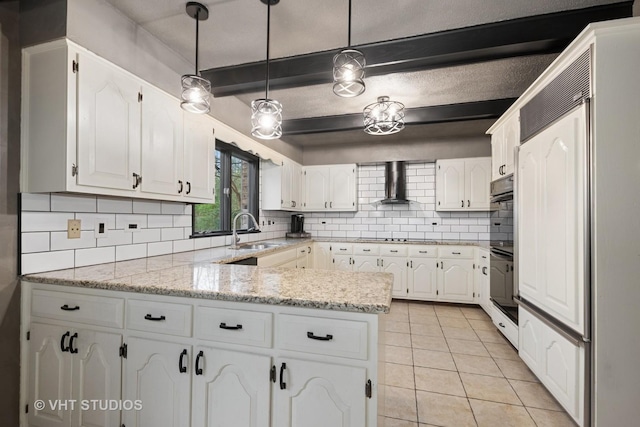 kitchen featuring a peninsula, wall chimney exhaust hood, white cabinetry, a sink, and light tile patterned floors
