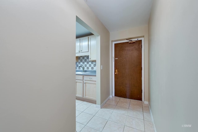 hallway featuring light tile patterned floors, a sink, and baseboards