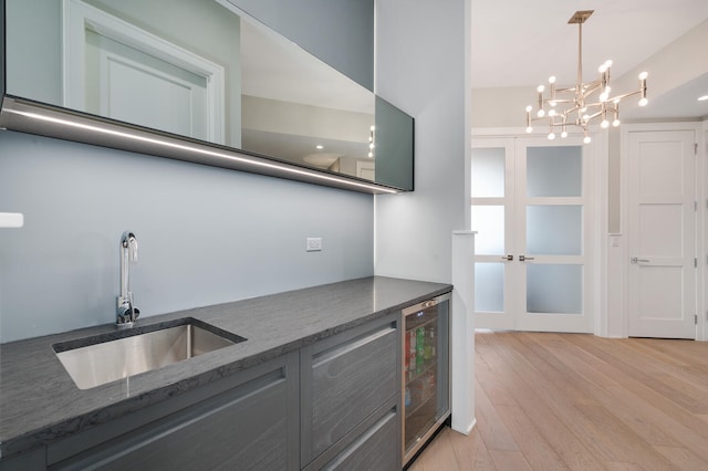 kitchen featuring an inviting chandelier, a sink, light wood-style floors, wine cooler, and french doors