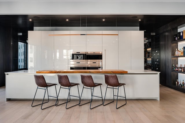 kitchen with modern cabinets, light wood finished floors, a breakfast bar area, and stainless steel double oven