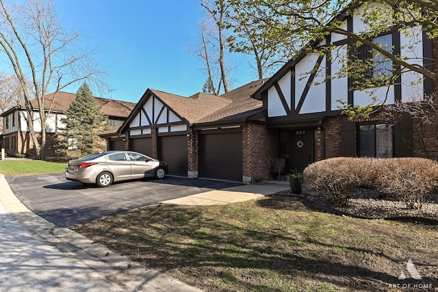 tudor home featuring roof with shingles, stucco siding, an attached garage, aphalt driveway, and brick siding