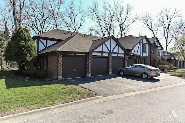tudor house with an attached garage, aphalt driveway, brick siding, a front yard, and a shingled roof