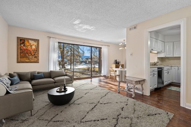 living area with dark wood-type flooring, visible vents, a chandelier, and a textured ceiling