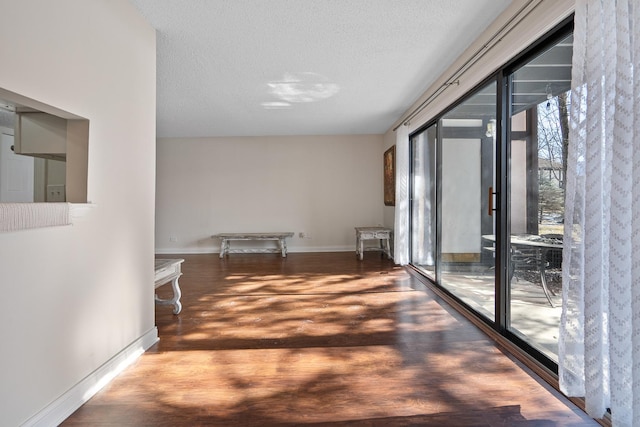 hallway featuring baseboards, a textured ceiling, and wood finished floors