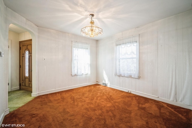 carpeted empty room with arched walkways, visible vents, an inviting chandelier, and a healthy amount of sunlight