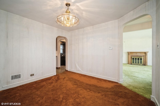 carpeted empty room with visible vents, baseboards, arched walkways, a chandelier, and a glass covered fireplace