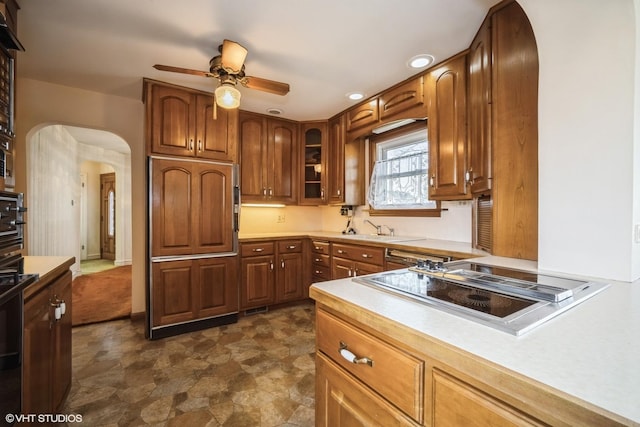 kitchen with arched walkways, a sink, light countertops, ceiling fan, and black electric stovetop