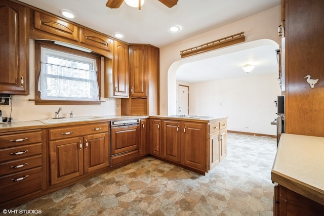 kitchen with brown cabinetry, arched walkways, ceiling fan, and a sink