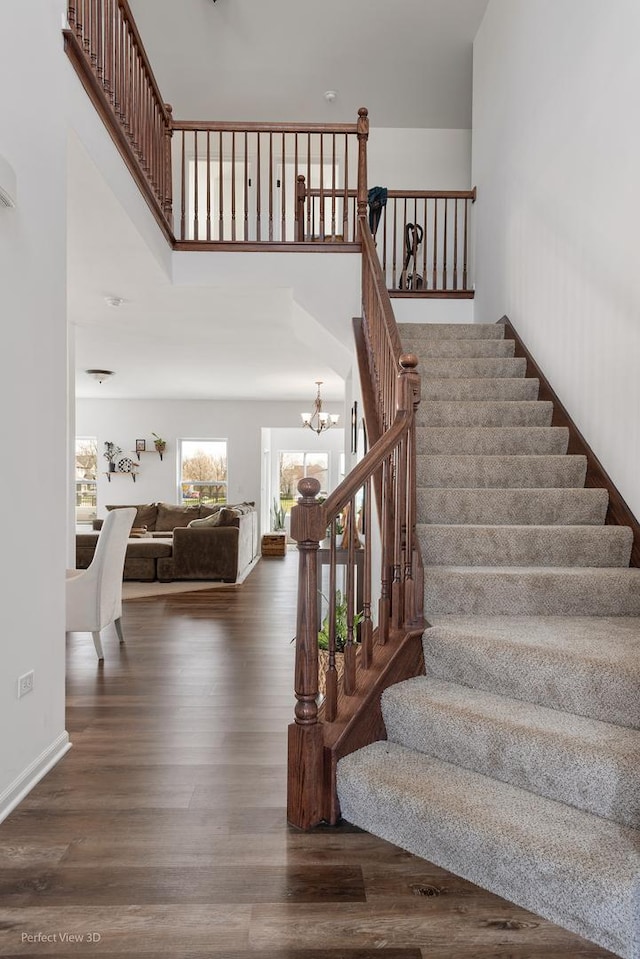 staircase with a chandelier, wood finished floors, a high ceiling, and baseboards
