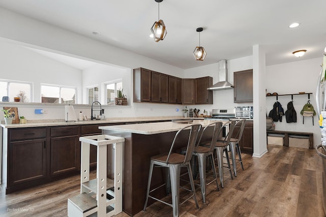 kitchen featuring wall chimney exhaust hood, a sink, dark brown cabinets, a kitchen island, and a breakfast bar area