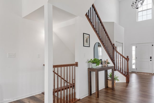 foyer with healthy amount of natural light, wood finished floors, a chandelier, stairway, and a high ceiling