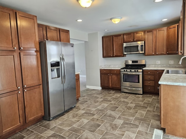 kitchen featuring recessed lighting, light countertops, a sink, stainless steel appliances, and baseboards