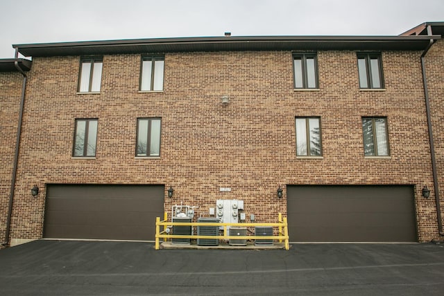 exterior space featuring a garage, aphalt driveway, and brick siding