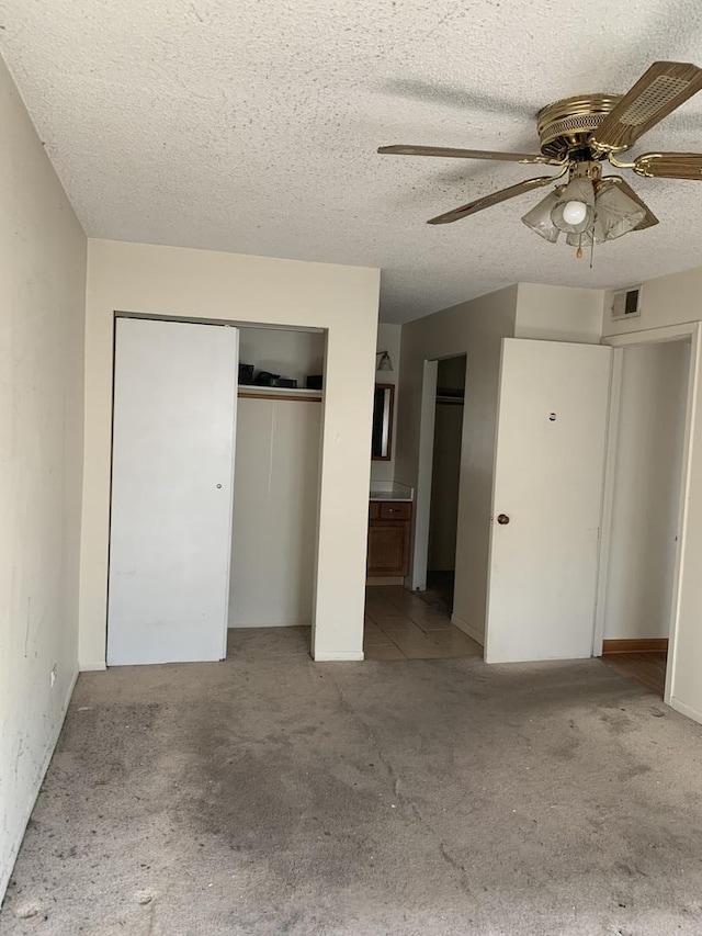 unfurnished bedroom featuring ensuite bathroom, a textured ceiling, a ceiling fan, visible vents, and carpet flooring