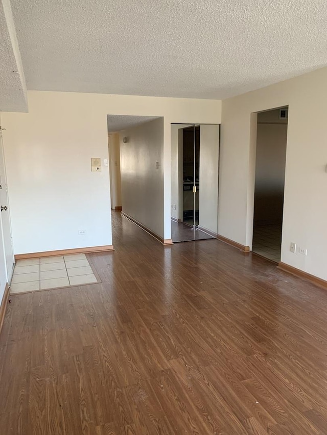 spare room featuring a textured ceiling, baseboards, and wood finished floors