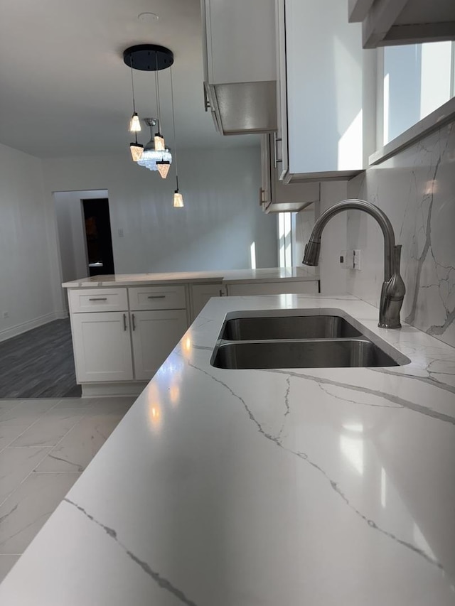 kitchen featuring light stone countertops, marble finish floor, a sink, hanging light fixtures, and decorative backsplash