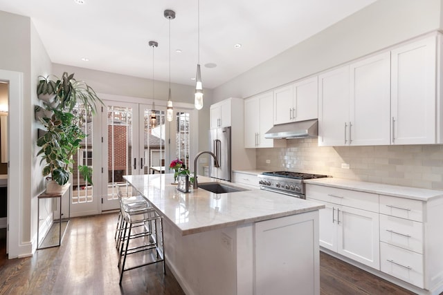 kitchen with under cabinet range hood, a sink, a center island with sink, high quality appliances, and backsplash