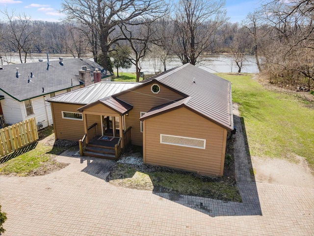 view of front of house featuring a water view, covered porch, metal roof, fence, and a front lawn