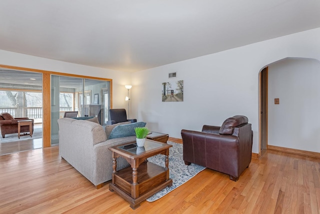 living room with arched walkways, baseboards, visible vents, and light wood-style floors